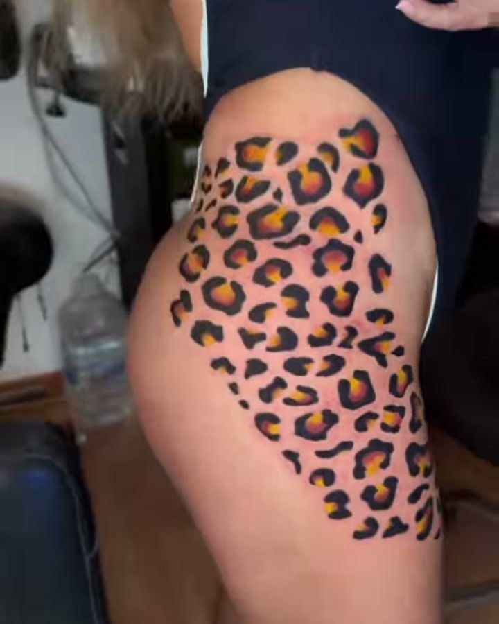 Tatuaje a color en la cadera y el muslo: estampado de piel de leopardo con manchas negras y centros anaranjados