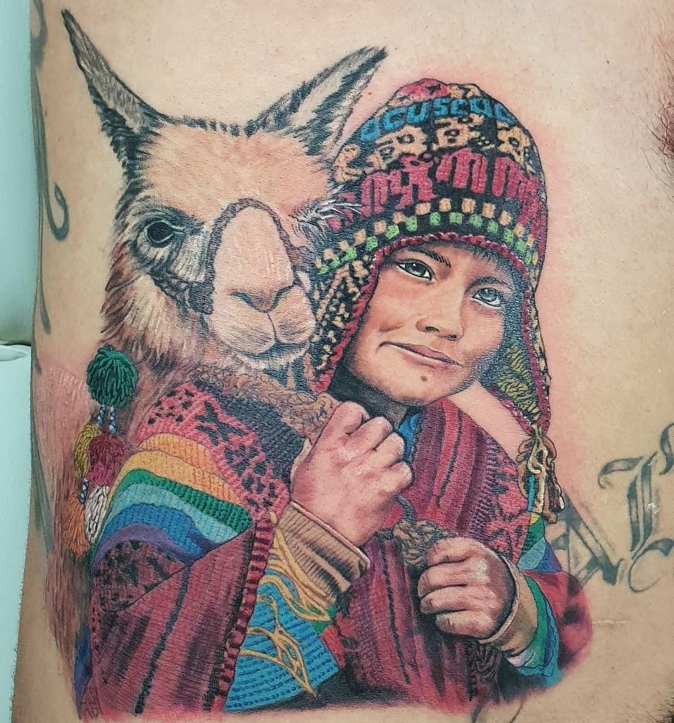 Tatuaje realista a color: niña andina con chullo y aguayo multicolor abrazando a una llama